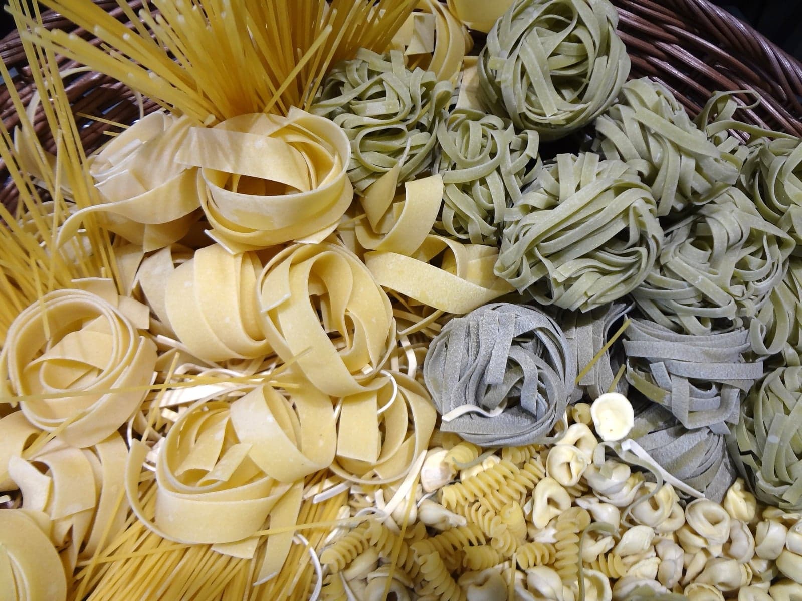 A wicker basket overflowing with many different shapes of dried pasta