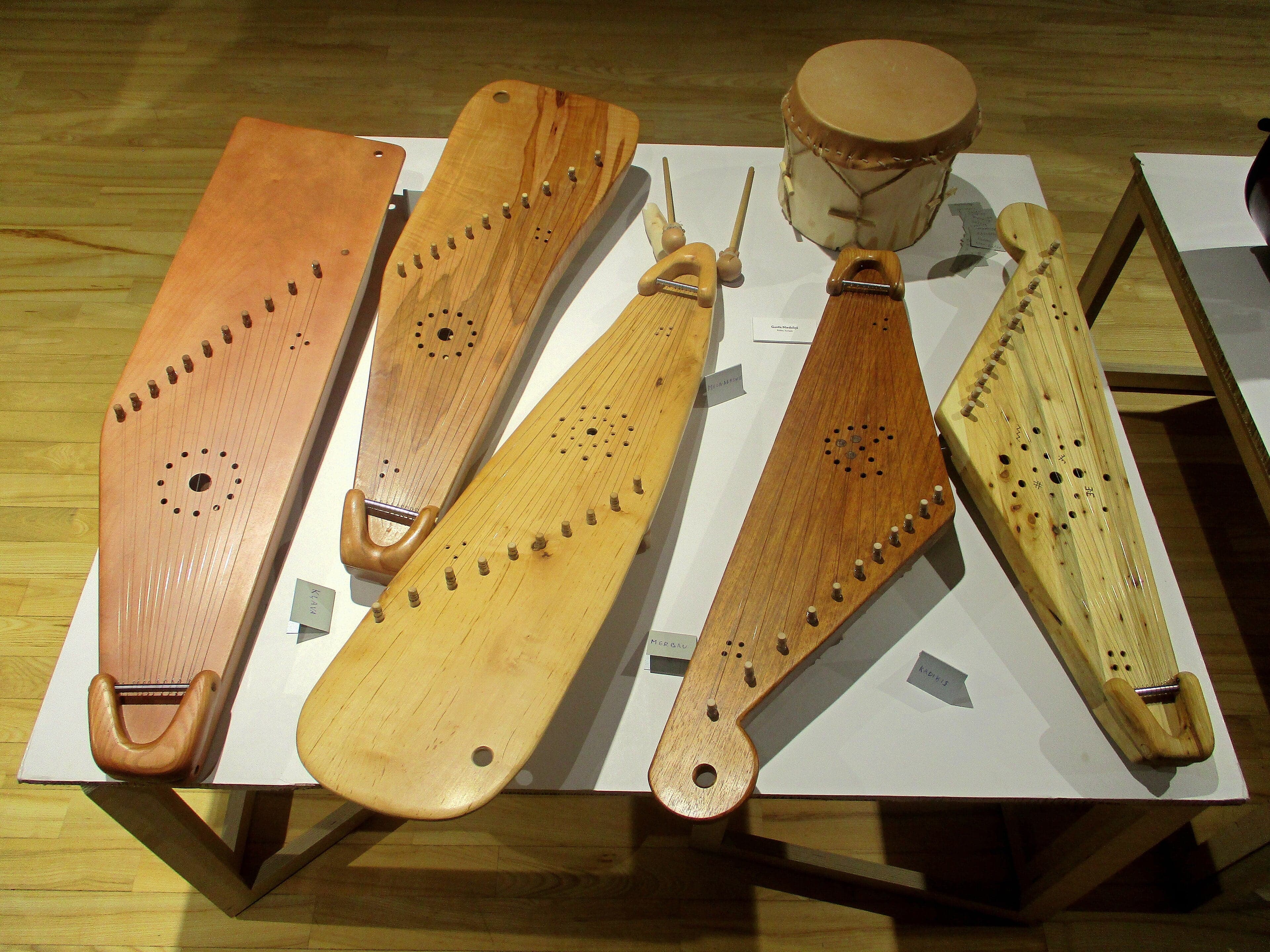 A carved wooden Latvian kokle instrument with strings resting on a wooden table