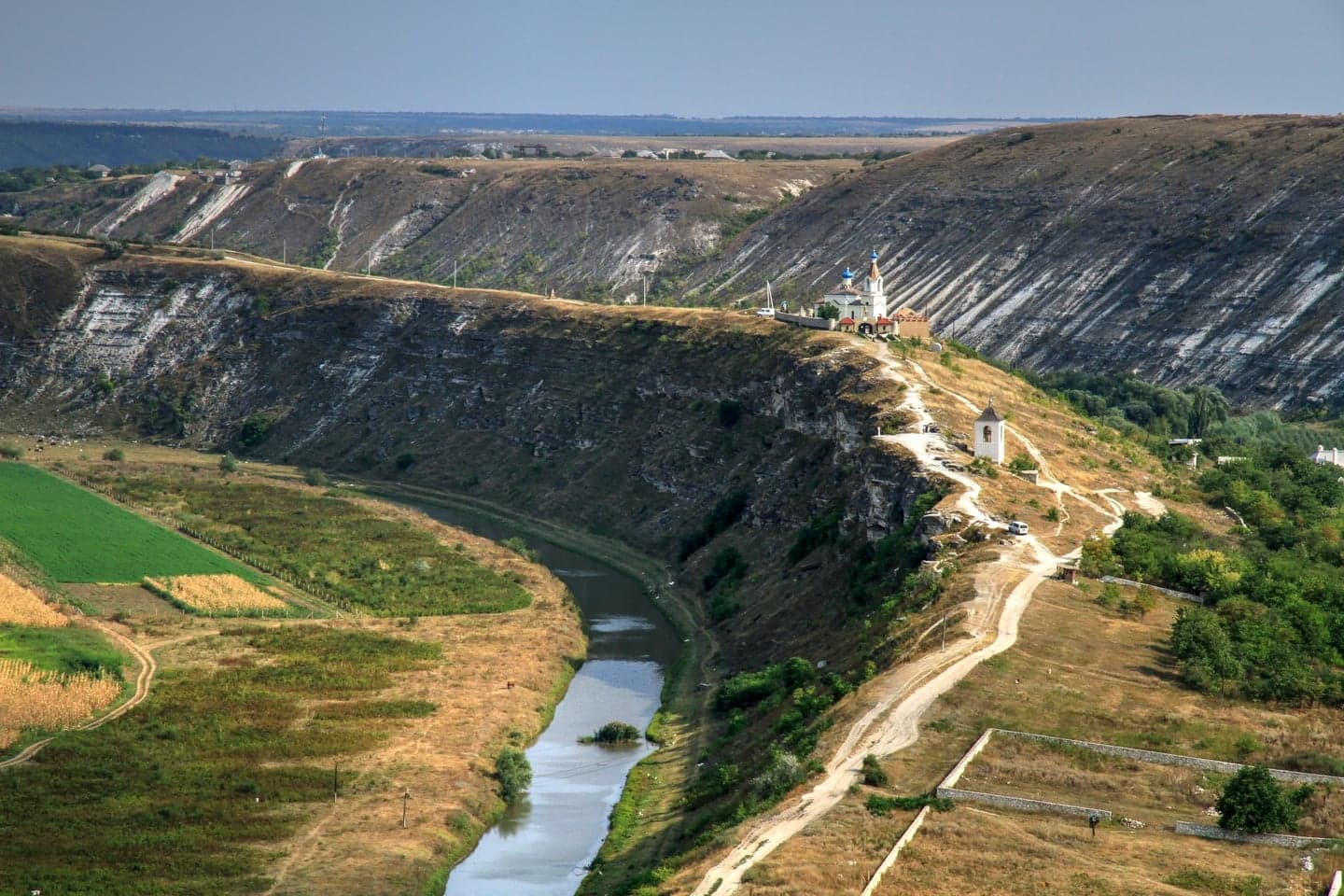 Carved cave rooms in the face of a limestone cliff above a winding river in Moldova