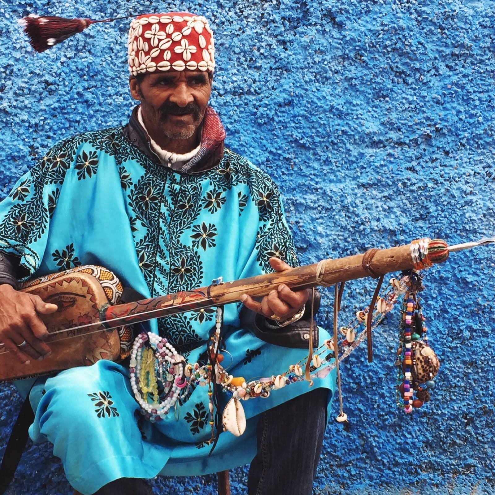 Gnawa musicians in colourful robes playing the guembri lute and clattering qraqeb