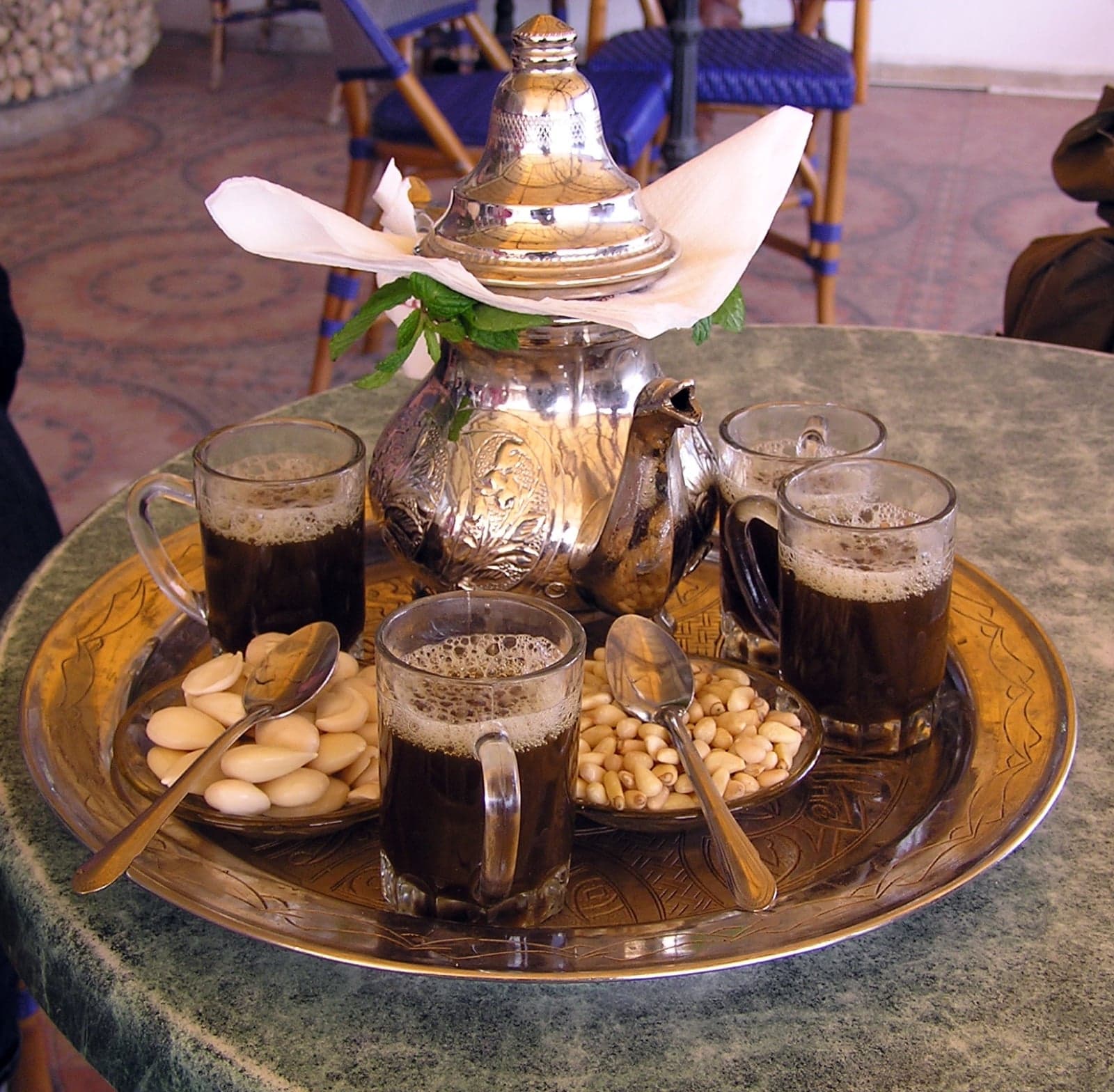 Hot mint tea being poured from a silver teapot held high above small glasses