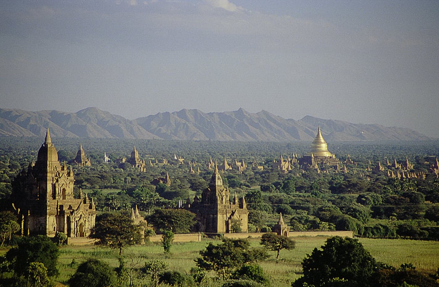 Brick temples rising out of green trees across the plain of Bagan at sunrise