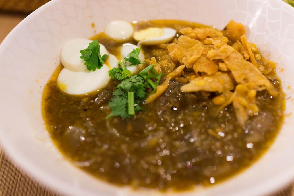 A bowl of mohinga - rice noodles in a yellow broth topped with crispy bits and a lemon wedge