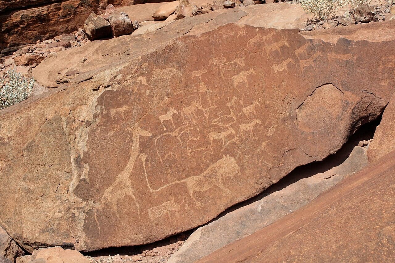 Ancient rock engravings of animals carved into a flat stone surface in a desert landscape