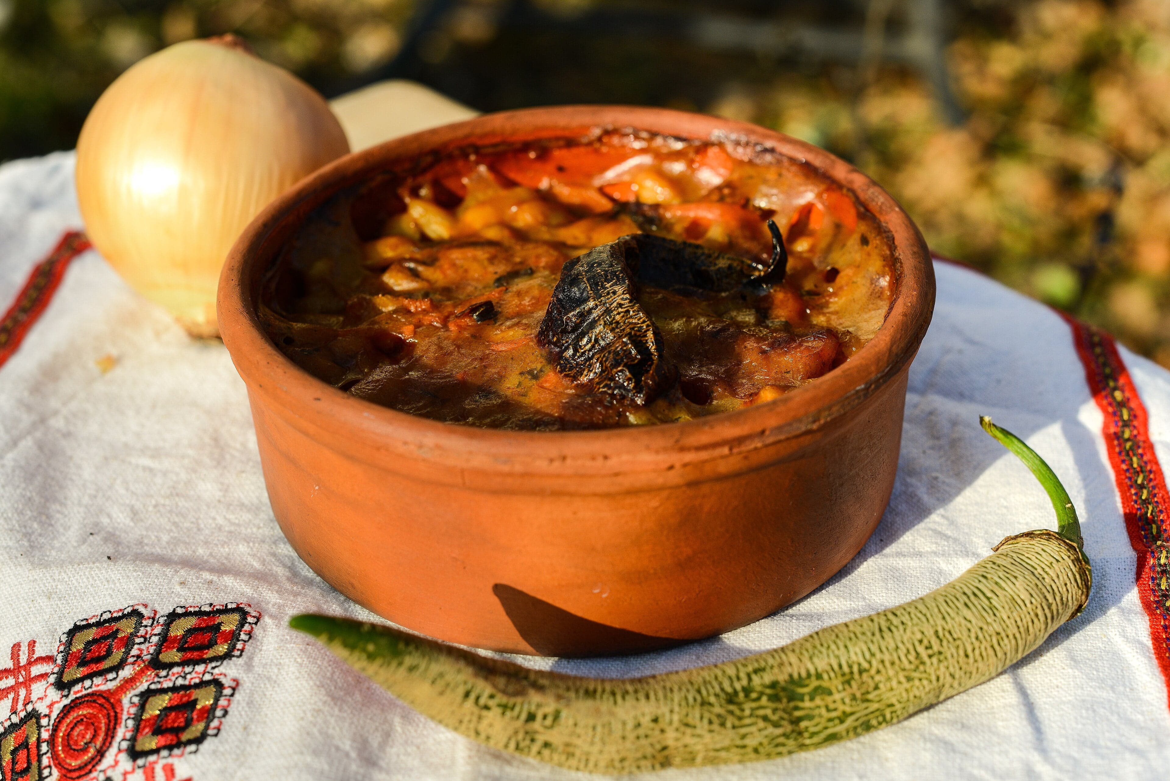 A clay pot of baked beans with a golden crust and herbs on top
