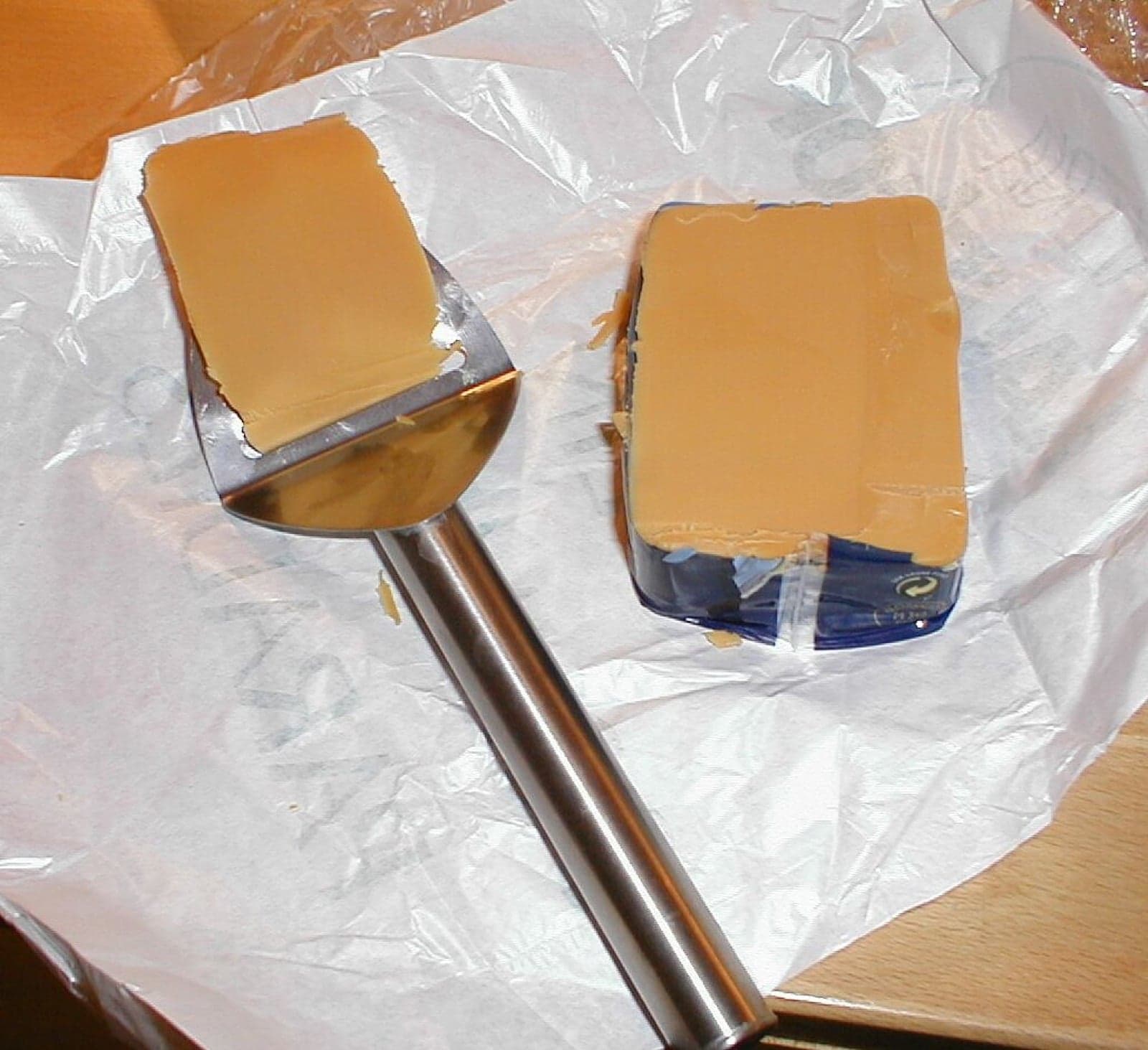 A slice of brunost on a slice of bread, with a Norwegian cheese slicer beside it