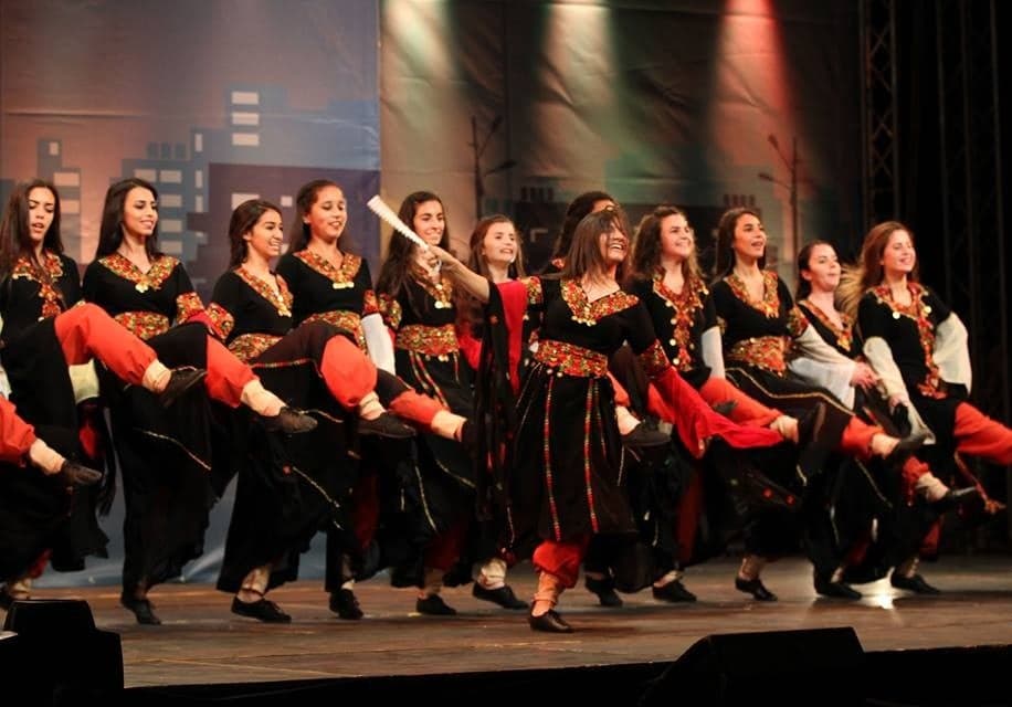 A line of young dancers in traditional dress performing dabke with arms linked