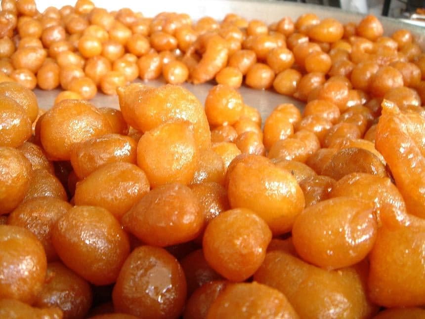A bowl of golden fried luqaimat balls drizzled with dark date syrup and sesame seeds