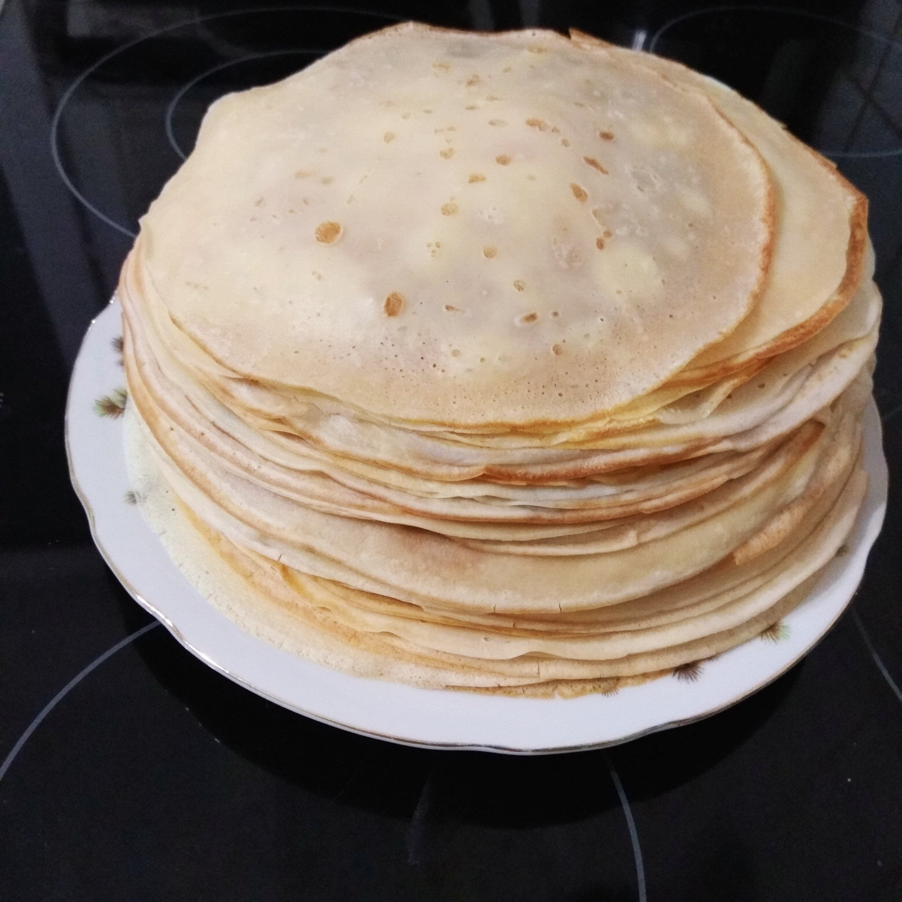 A stack of thin golden Russian blini pancakes on a plate with sour cream and jam