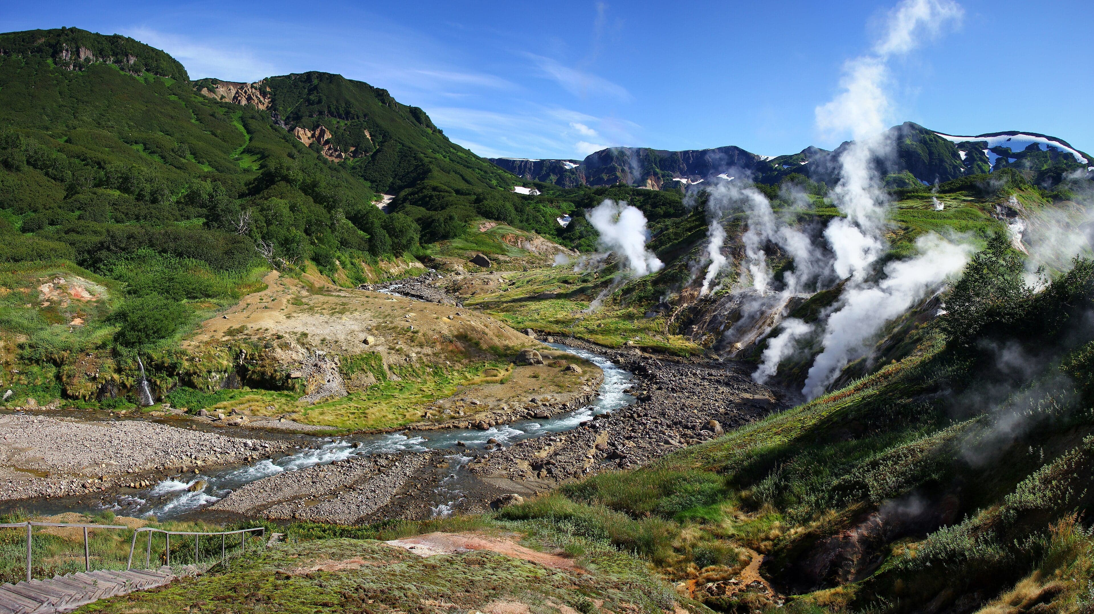 Steaming geysers erupt in a valley surrounded by snow-capped volcanoes in Kamchatka