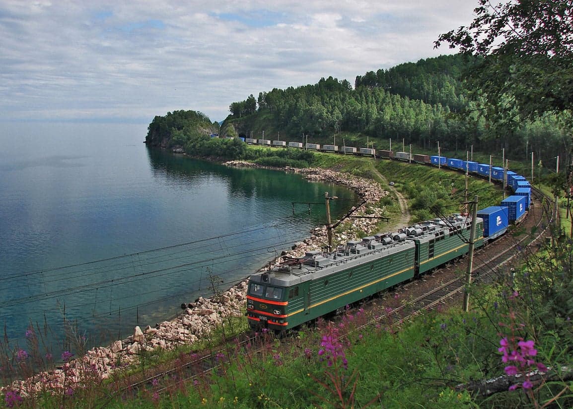 A train travelling through snowy Siberian forest alongside a frozen river
