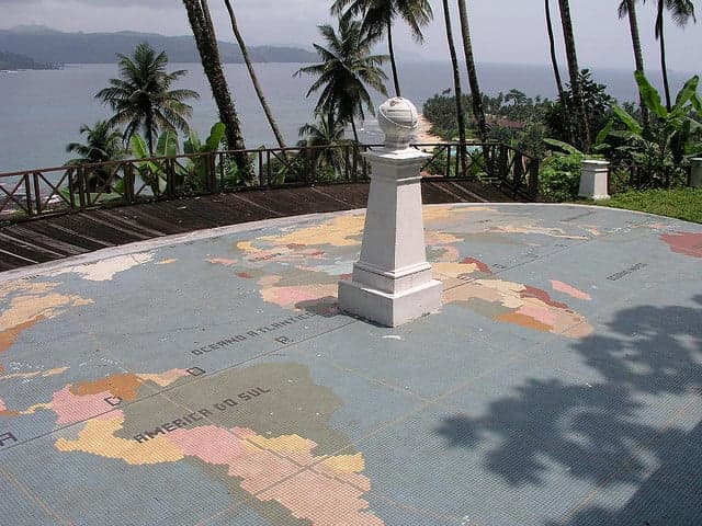 The white Equator Monument marker on São Tomé island with the ocean in the background