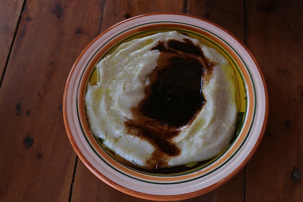 Thin sheets of kisra flatbread on a woven mat next to a bowl of asida porridge