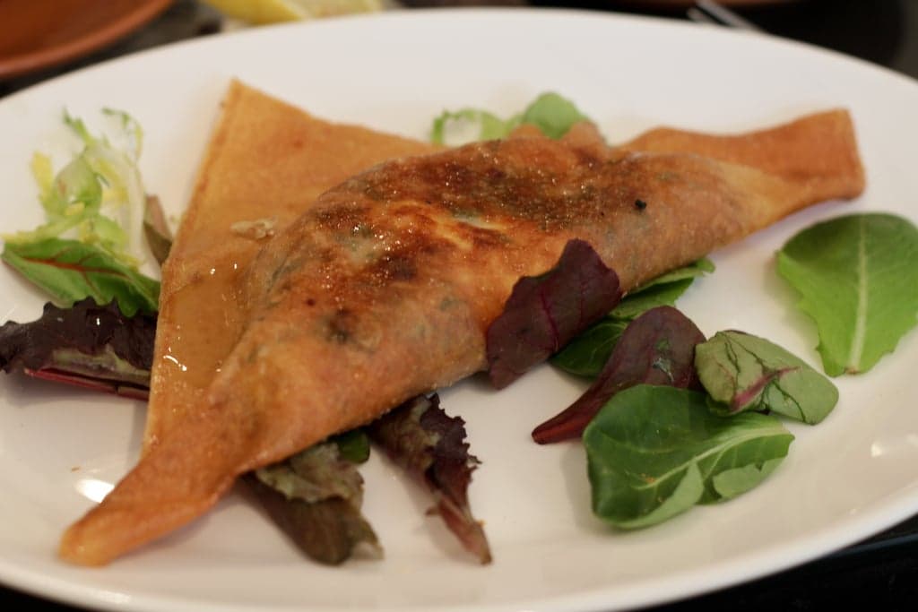 A golden crispy brik pastry on a plate with a squeeze of lemon beside it