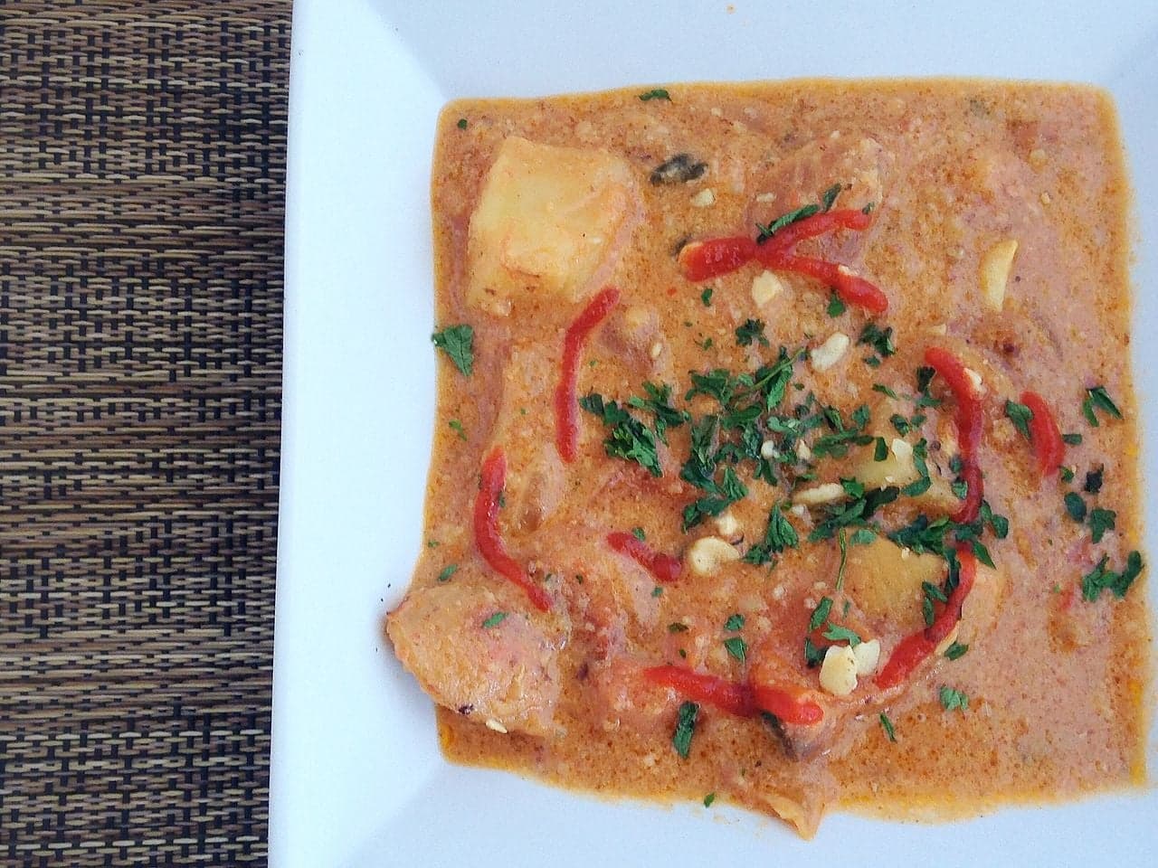 A bowl of creamy brown groundnut sauce next to a plate of matoke